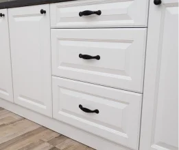 White raised-panel kitchen drawers and doors with black handles and a dark benchtop